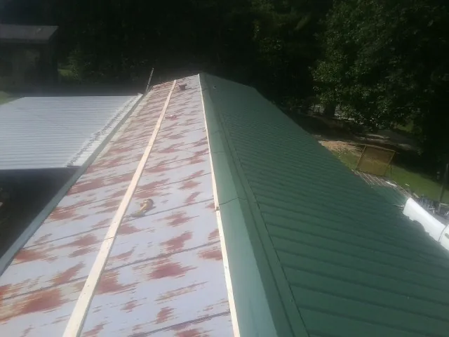 Old rusted panels beside newly installed green metal roofing — Wind Damage Roof Repair by Roofing Brothers in Mineral