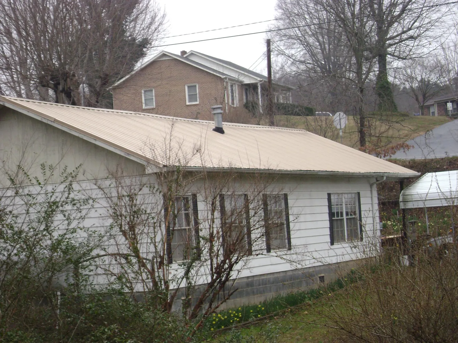Tan metal roof on a white sided house set into a hillside — Commercial Roofing by Roofing Brothers in Mineral